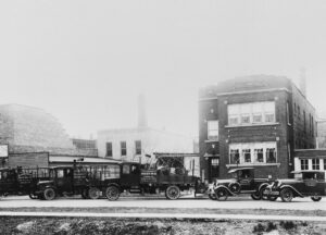 A photo of Allendorfer Contractors in Chicago from 1885 including several roofing trucks and Model-T style cars in front of an apartment building.